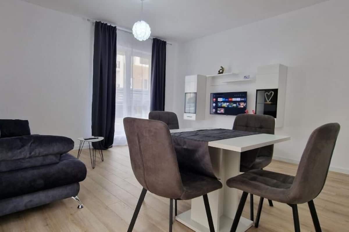 A modern living room with a sofa, chairs, a dining table, and a TV mounted on the wall.