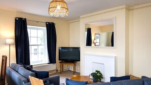 Un salon comprenant un ensemble de canapés, un téléviseur, une cheminée et une grande fenêtre avec des rideaux.