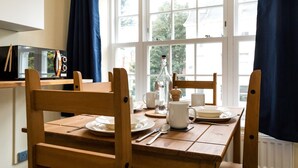 Une table à manger est dressée avec des assiettes, des tasses et une bouteille, placée devant une fenêtre ornée de rideaux.