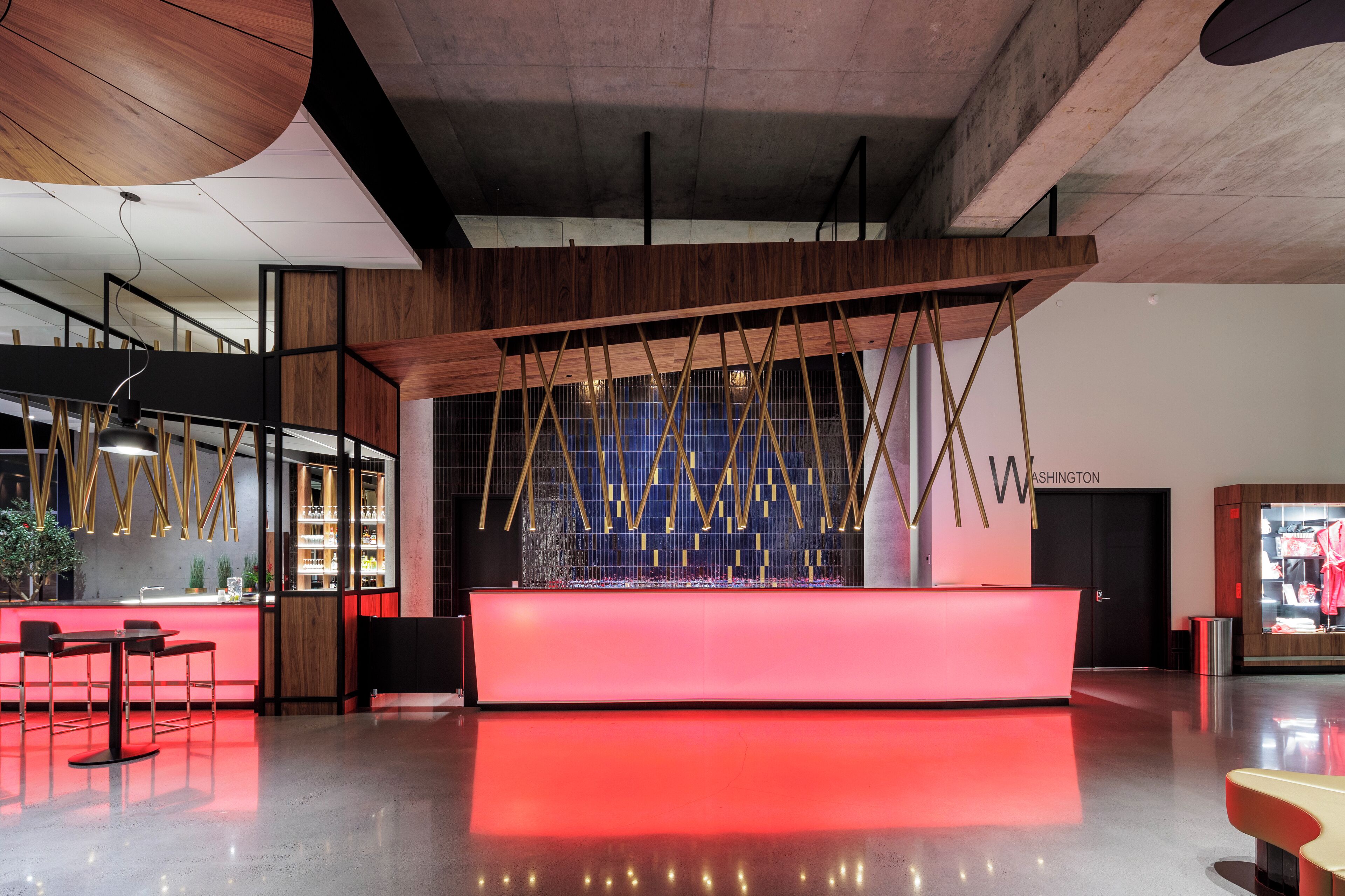 A modern reception area with a red-lit counter, wooden accents, and a geometric light installation.