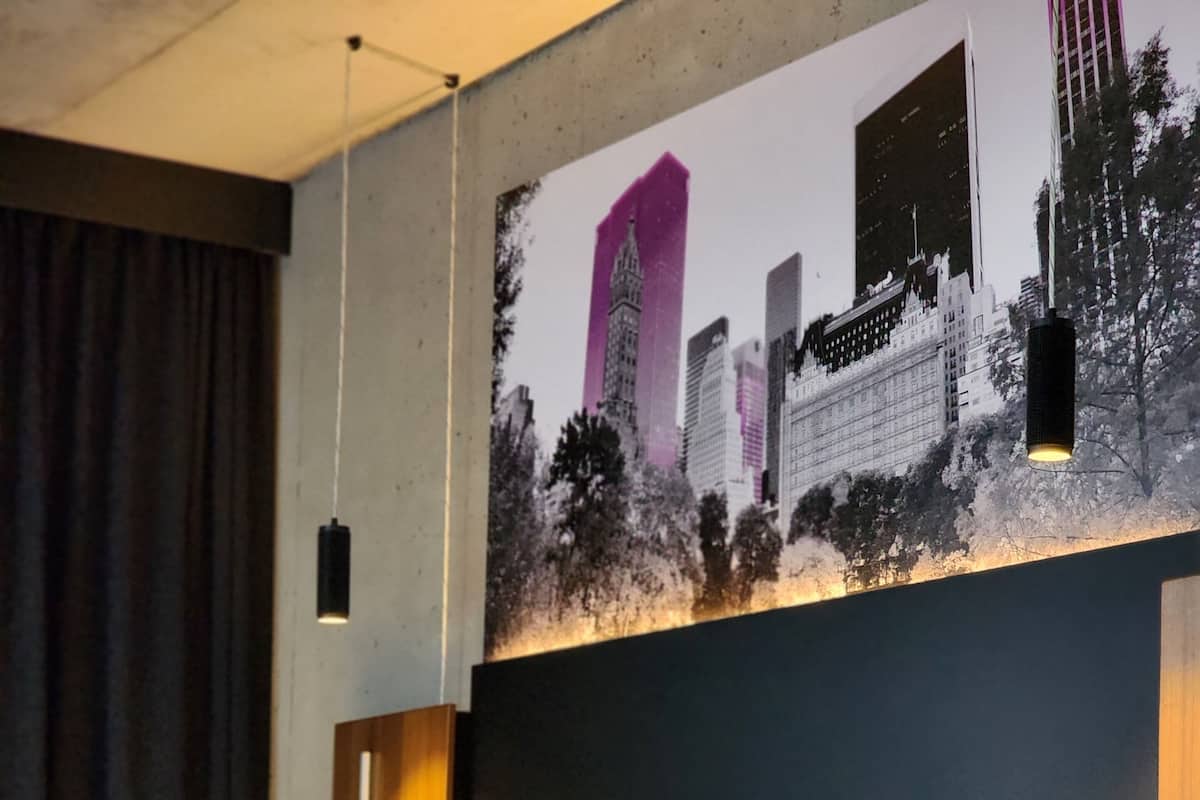 A hotel room with a bed, pillows, a headboard, a wall-mounted artwork, and a nightstand.