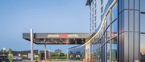 A modern Grand Times Hotel entrance with a covered walkway, glass facade, and a clear sky.