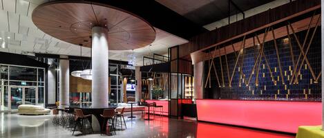 A modern interior with a red-lit reception desk, high ceilings, and contemporary furniture.