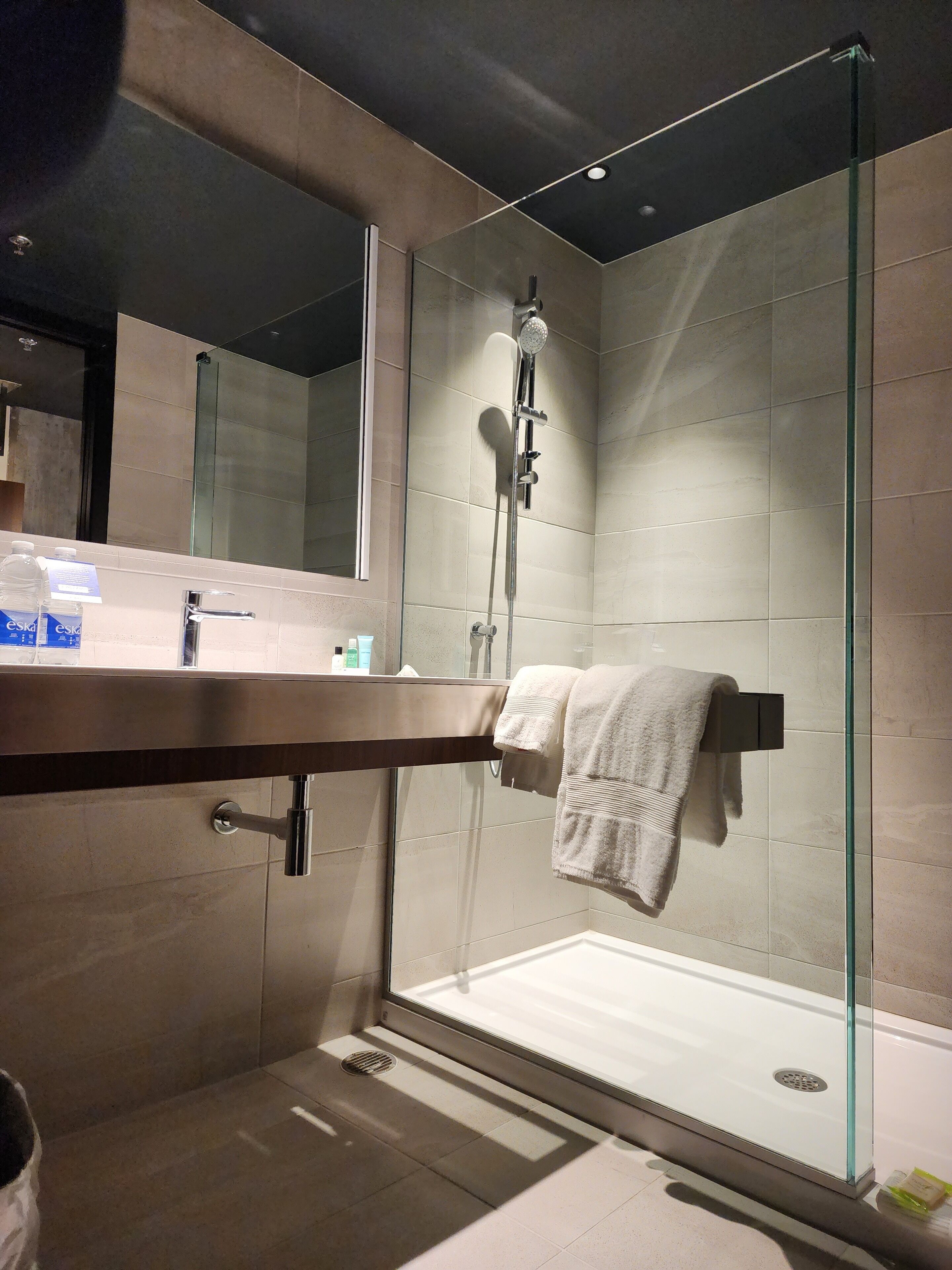 A modern bathroom with a glass-enclosed shower, a vanity with a mirror, and a towel rack.