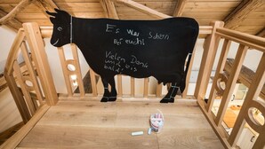 A black cow-shaped decoration with text in a room with wooden beams and a wooden railing. - Ferienwohnung Josefine (Münster Albachten)