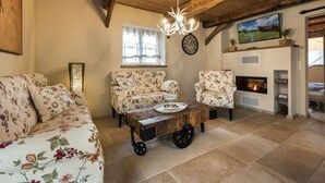 A rustic living room with a wooden ceiling, floral sofas, a coffee table with wheels, a fireplace, and a clock on the wall. - Ferienwohnung Josefine (Münster Albachten)