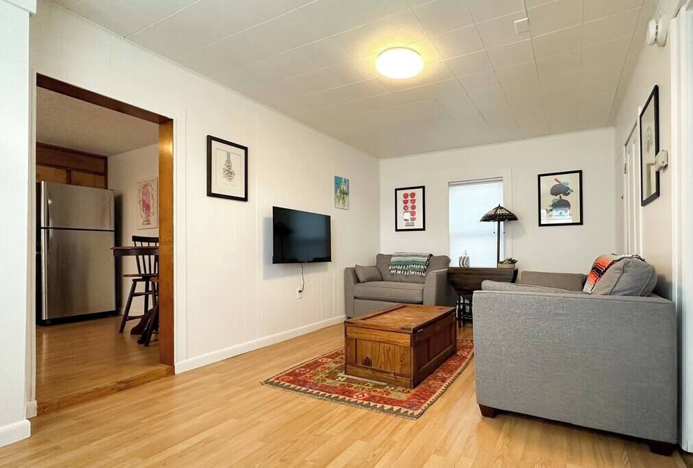 Un salon avec un canapé gris, une table basse en bois et un téléviseur fixé au mur.