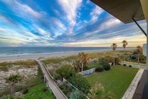 Vista a la playa desde un balcón con terraza de madera, palmeras y una zona ajardinada.