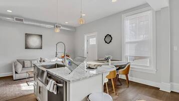A modern kitchen with a central island, a dining area with a table and chairs, and a living space with a sofa.