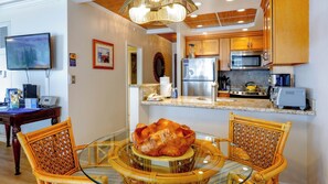 A modern kitchen with a central island, wooden cabinets, stainless steel appliances, and a dining area with wicker chairs.