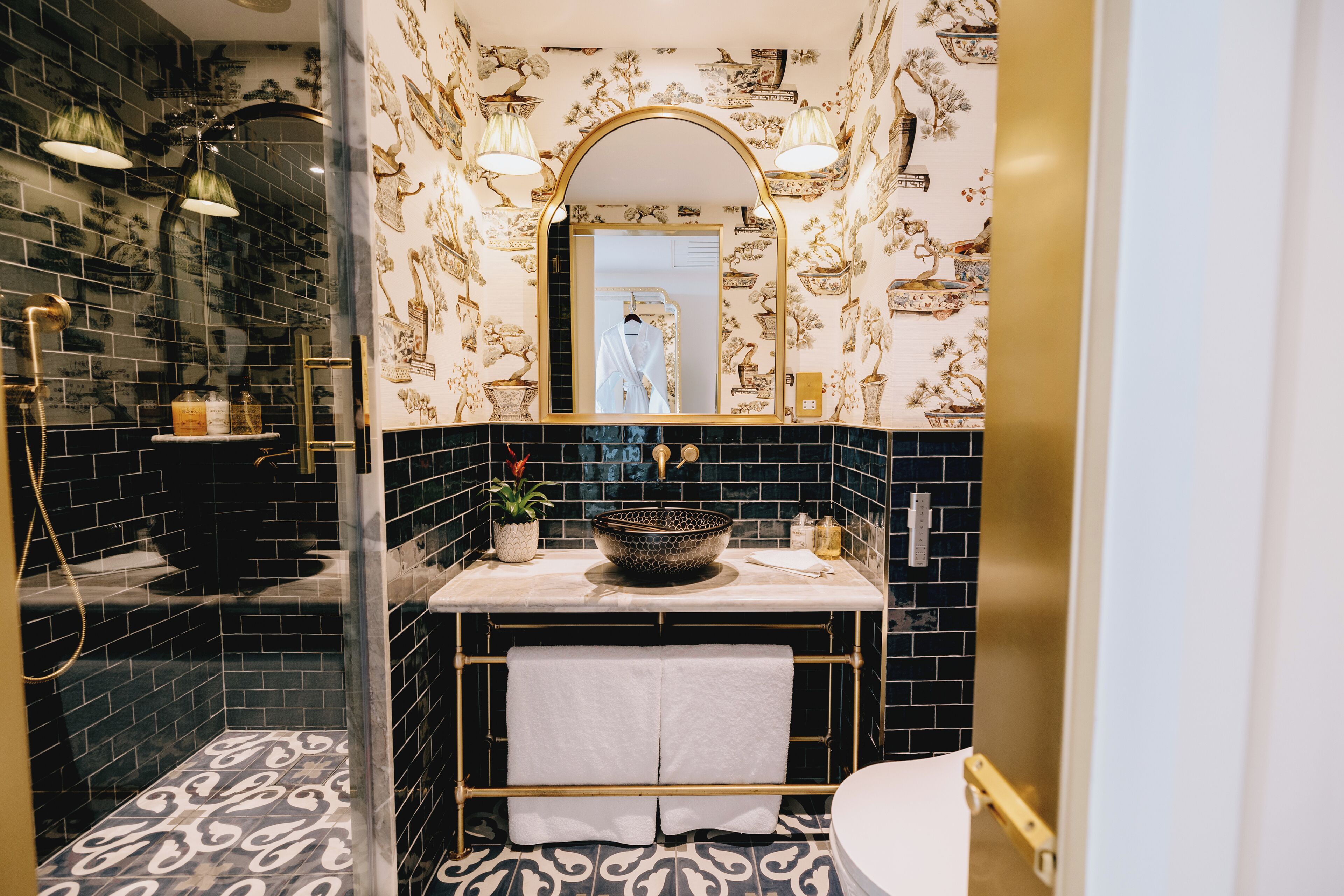 Un baño con suelo estampado en blanco y negro, un lavabo con un cuenco decorativo y un espejo con marco arqueado.