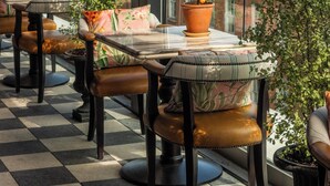 A terrace with tables and chairs, potted plants, and a view of buildings through large windows. - The Leinster (Dublin)