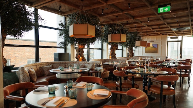 A spacious restaurant with high ceilings, large windows, and a mix of round and rectangular tables. - The Leinster (Dublin)