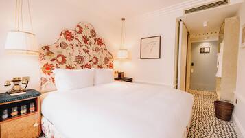 Una habitación de hotel con una cama grande, una mesita de noche con lámpara, un cabecero floral y una alfombra estampada.