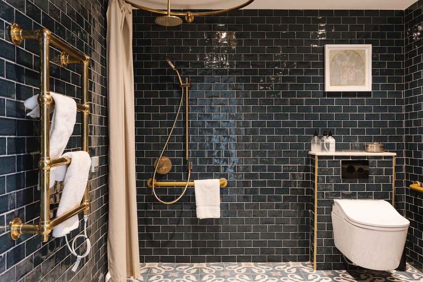 Un baño con paredes de azulejos oscuros, sistema de ducha dorado, inodoro y estante con artículos de aseo.