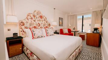 A hotel room with a large bed, a red armchair, a wooden desk, and a view of the outside.