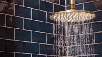 Una ducha con accesorios dorados y agua corriendo por una pared de azulejos.