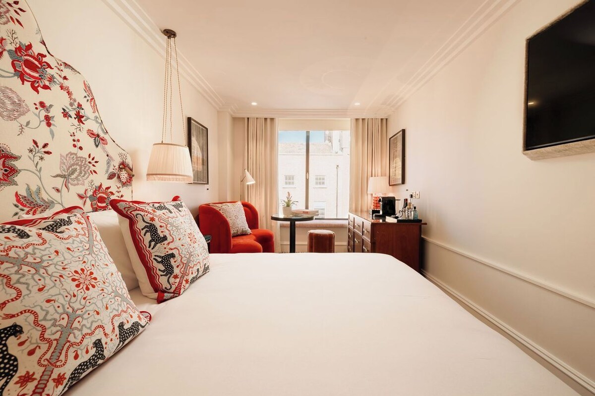 A hotel room with a large bed, a red armchair, a small table, and a TV mounted on the wall.