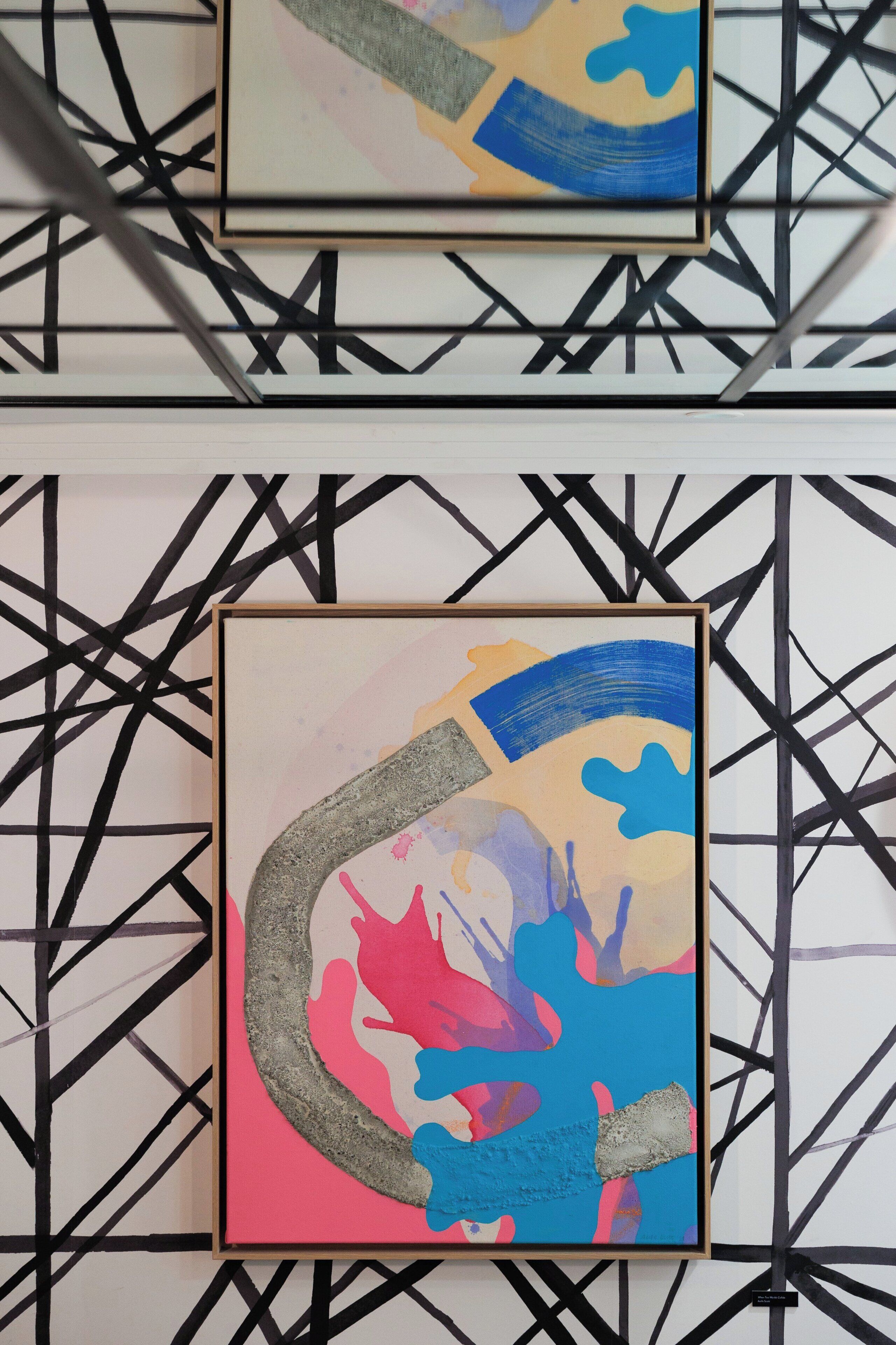 Deux tableaux abstraits encadrés sont accrochés à un mur orné d’un motif géométrique.