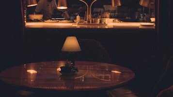 A dimly lit restaurant with a neon sign reading "Cha Cha" and a view of the kitchen through a window.