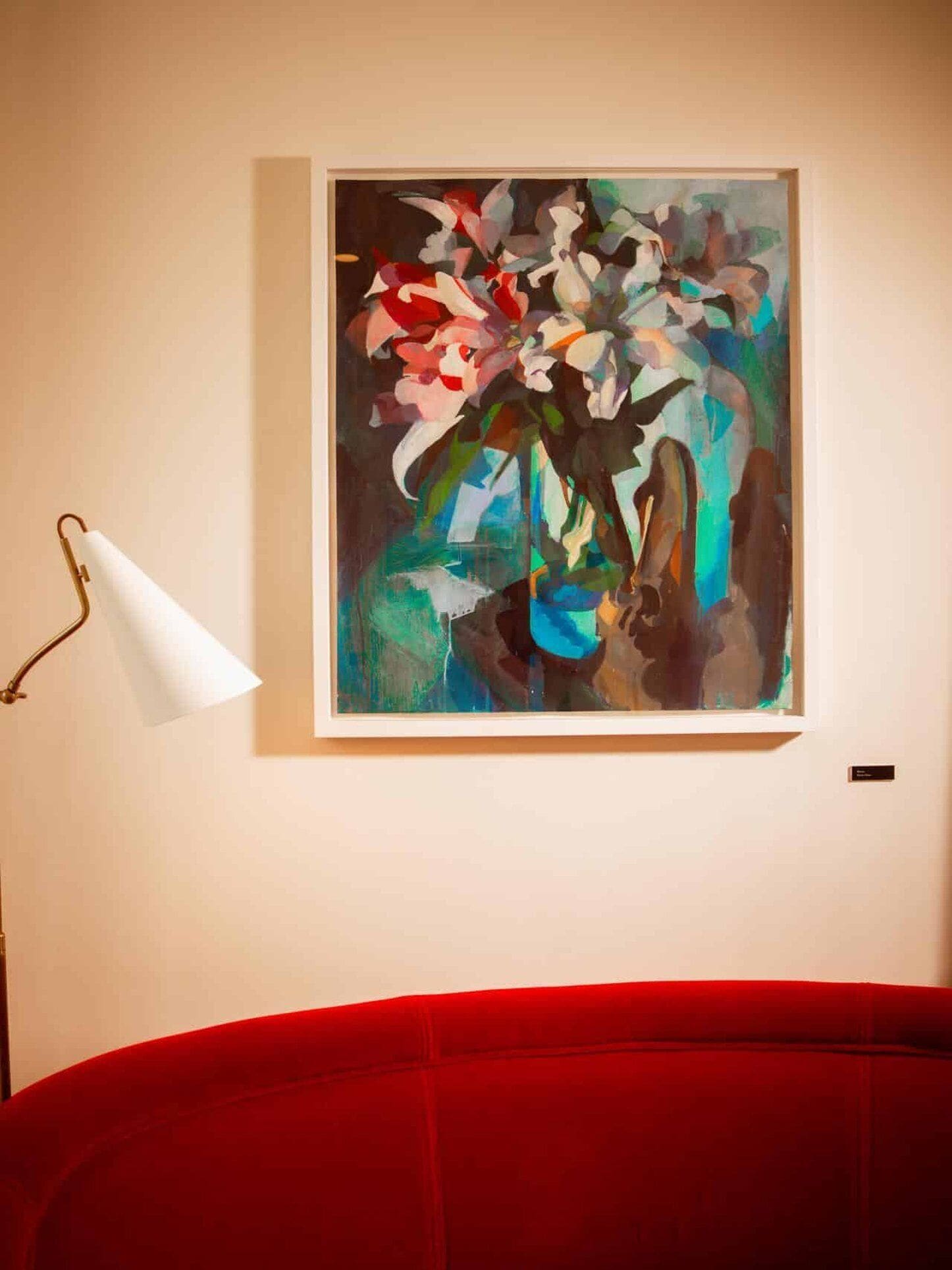 Un cuadro abstracto enmarcado en una pared, una lámpara de pie blanca y un sofá rojo.