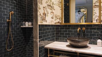 A bathroom with a black tiled wall, a gold showerhead, a sink with a patterned bowl, and a mirror with a gold frame.