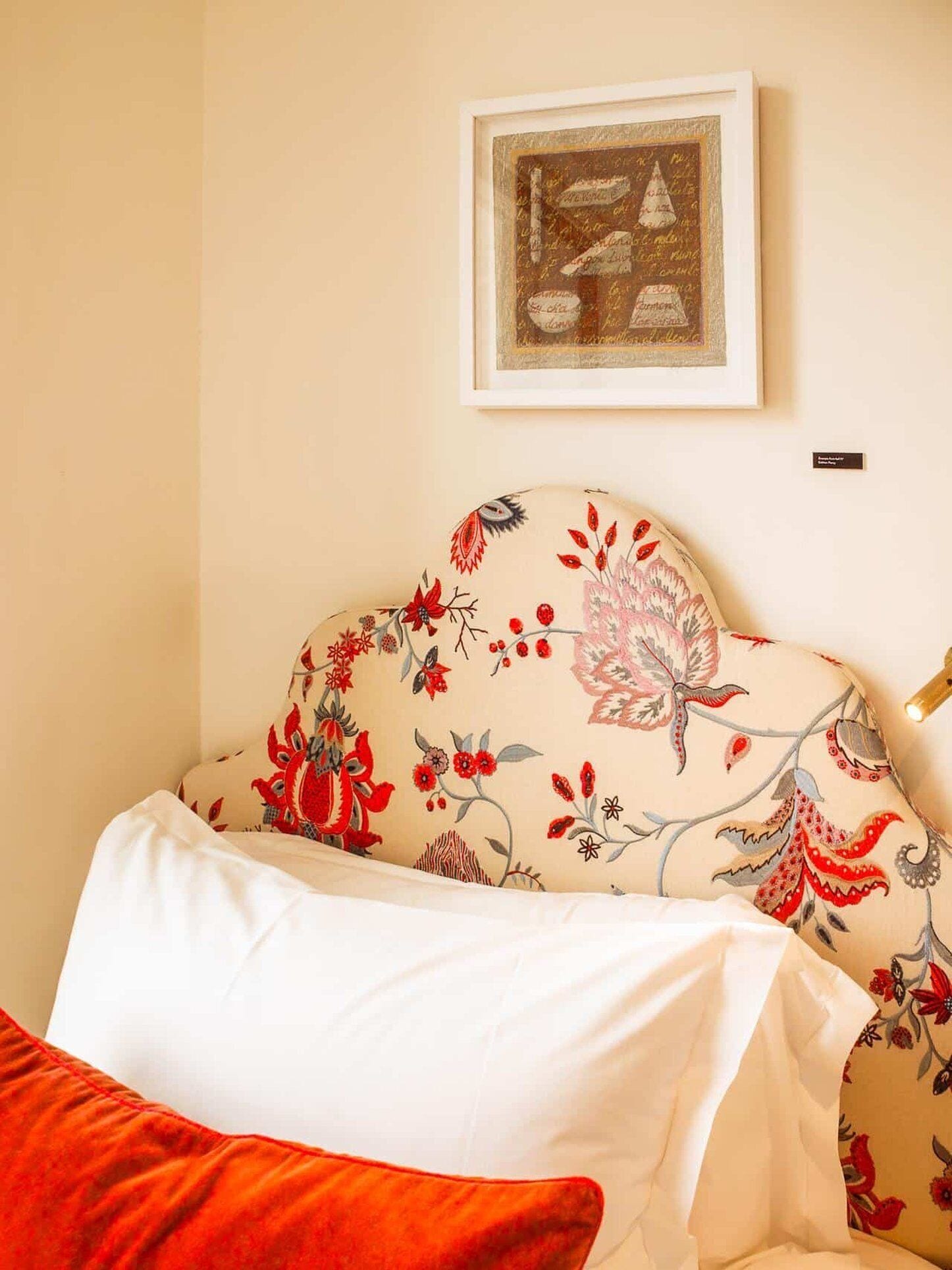 A bedroom with a floral-patterned headboard, a white bedspread, and a red pillow.