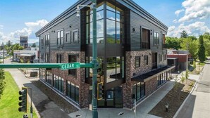 A modern multi-story building with a prominent corner entrance, large windows, and a visible street sign reading "CEDAR ST."