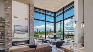 A modern living room with a fireplace, large windows, and a dining area.