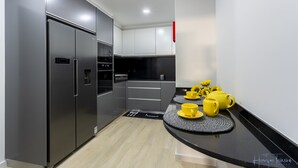 A modern kitchen with a stainless steel refrigerator, black and white cabinets, and a black countertop. - Charming 3-bed House in Funchal (Funchal)