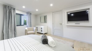 A modern bedroom with a bed, a TV, a dresser, and a window with curtains. - Charming 3-bed House in Funchal (Funchal)