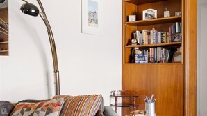 A living room with a sofa, a wooden side table, a floor lamp, and a bookshelf.