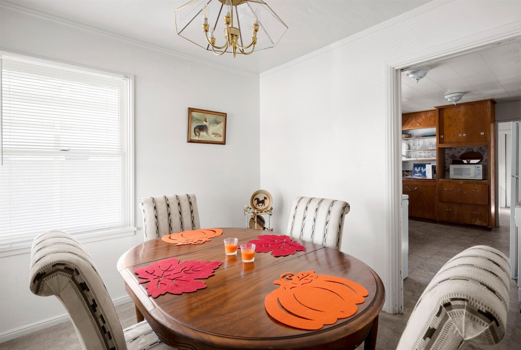Een eetkamer met een houten tafel, streepstoelen en placemats met een herfstthema.