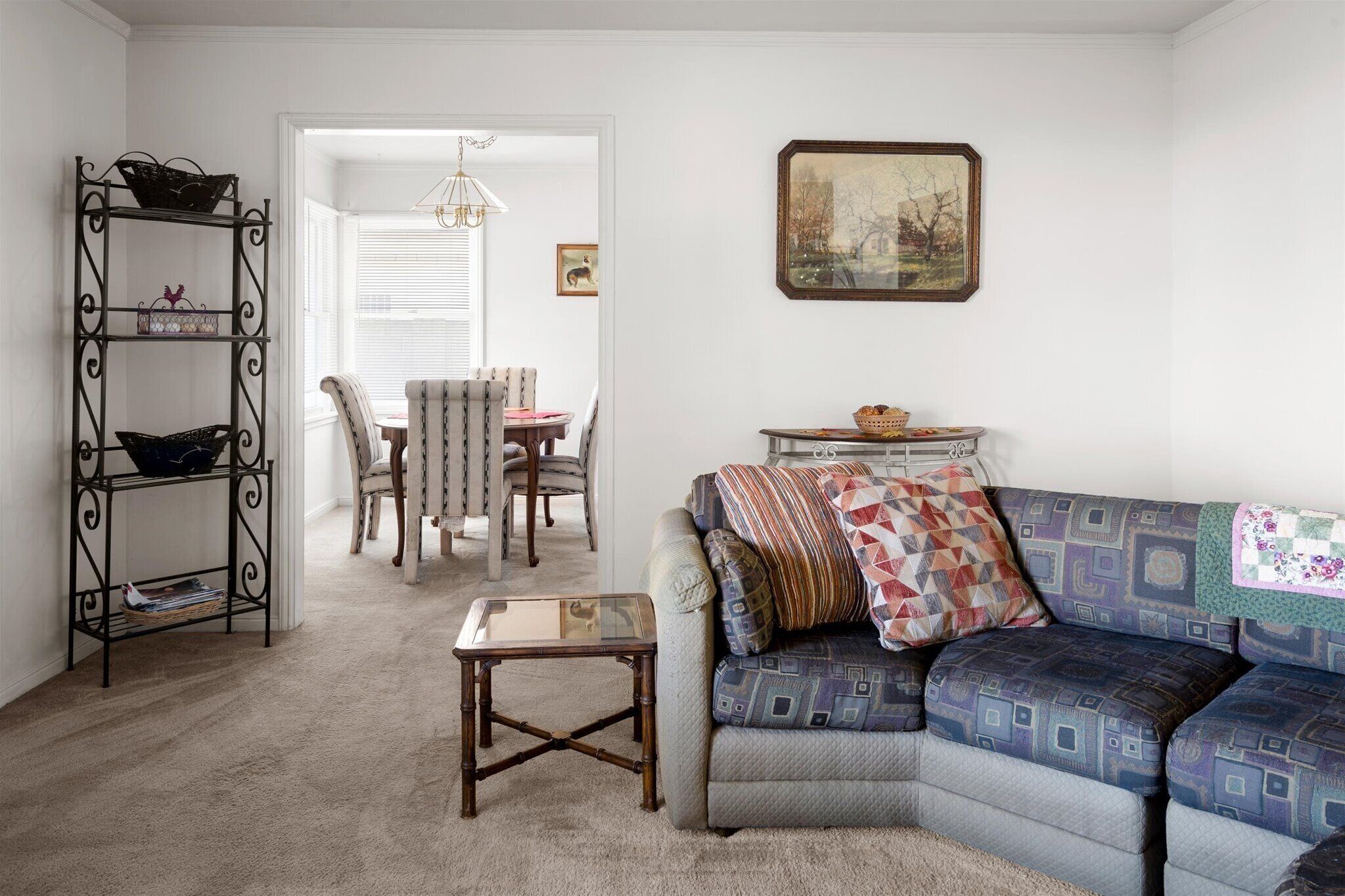 A living room with a sofa, a coffee table, a bookshelf, and a dining area with chairs and a table.