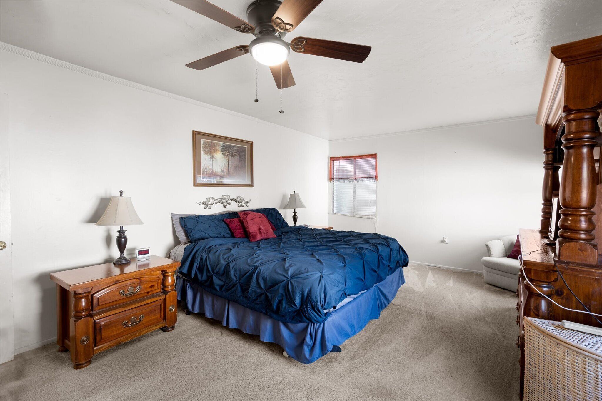 A bedroom with a bed, nightstand, dresser, ceiling fan, and a window with blinds.