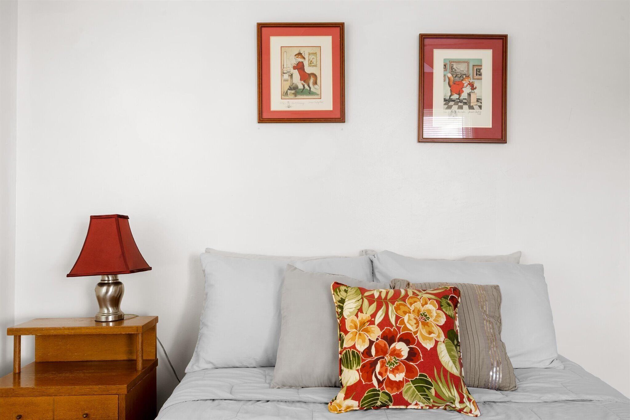 A bedroom with a bed, pillows, a nightstand, a lamp, and two framed pictures on the wall.