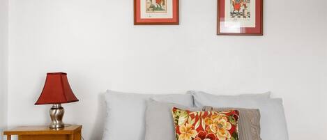 A bedroom with a bed, pillows, a nightstand, a lamp, and two framed pictures on the wall.