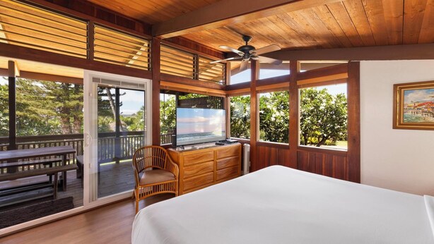 A bedroom with a large bed, wooden desk, and a view of the outdoors.