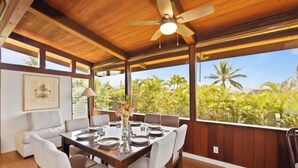 A dining area with a wooden ceiling, large windows, and a view of palm trees.