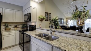 A kitchen with granite countertops, stainless steel appliances, and white cabinetry. There are plants and a vase on the counter. - Updated luxury 2 BR Lake Forest in Sea Pines Bikes & Beach Gear included (Hilton Head Island)