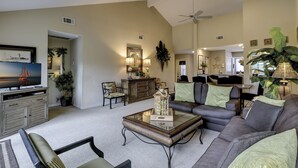 A spacious living room with a large sofa, a coffee table, and a television. There are several chairs and a dining area in the background. - Updated luxury 2 BR Lake Forest in Sea Pines Bikes & Beach Gear included (Hilton Head Island)