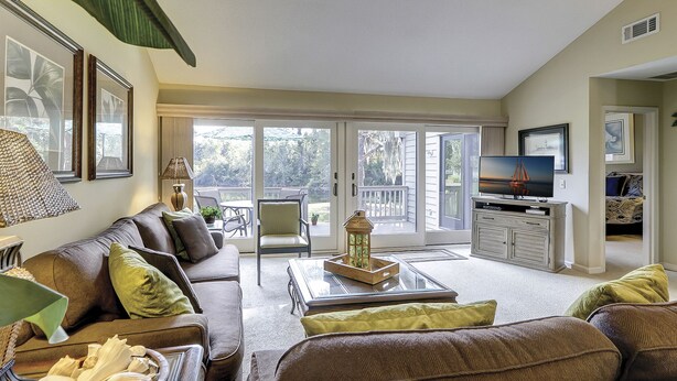 A living room with a sofa, coffee table, and TV. There is a sliding glass door leading to a balcony. - Updated luxury 2 BR Lake Forest in Sea Pines Bikes & Beach Gear included (Hilton Head Island)