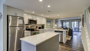 A modern kitchen with stainless steel appliances, a central island, and a dining area with a view of the outdoors. - Updated New Luxury Vacation Condo w New Kitchen Bikes & Beach Gear included (Hilton Head Island)