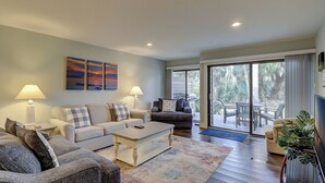 A living room with a sofa, coffee table, and a TV. There is a sliding glass door leading to a patio with outdoor furniture. - Updated New Luxury Vacation Condo w New Kitchen Bikes & Beach Gear included (Hilton Head Island)