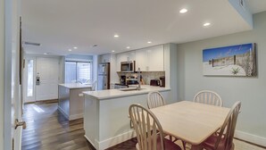 A modern kitchen with white cabinets, a central island, and a dining area with wooden chairs. - Updated New Luxury Vacation Condo w New Kitchen Bikes & Beach Gear included (Hilton Head Island)