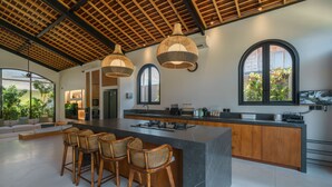 A modern kitchen with a large island, bar stools, and pendant lighting. - Casa Donilo  (Canggu)