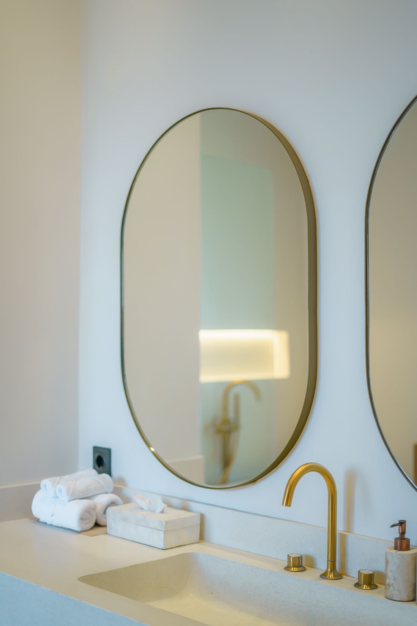 Une salle de bain avec un grand miroir ovale, un robinet doré et un lavabo blanc.