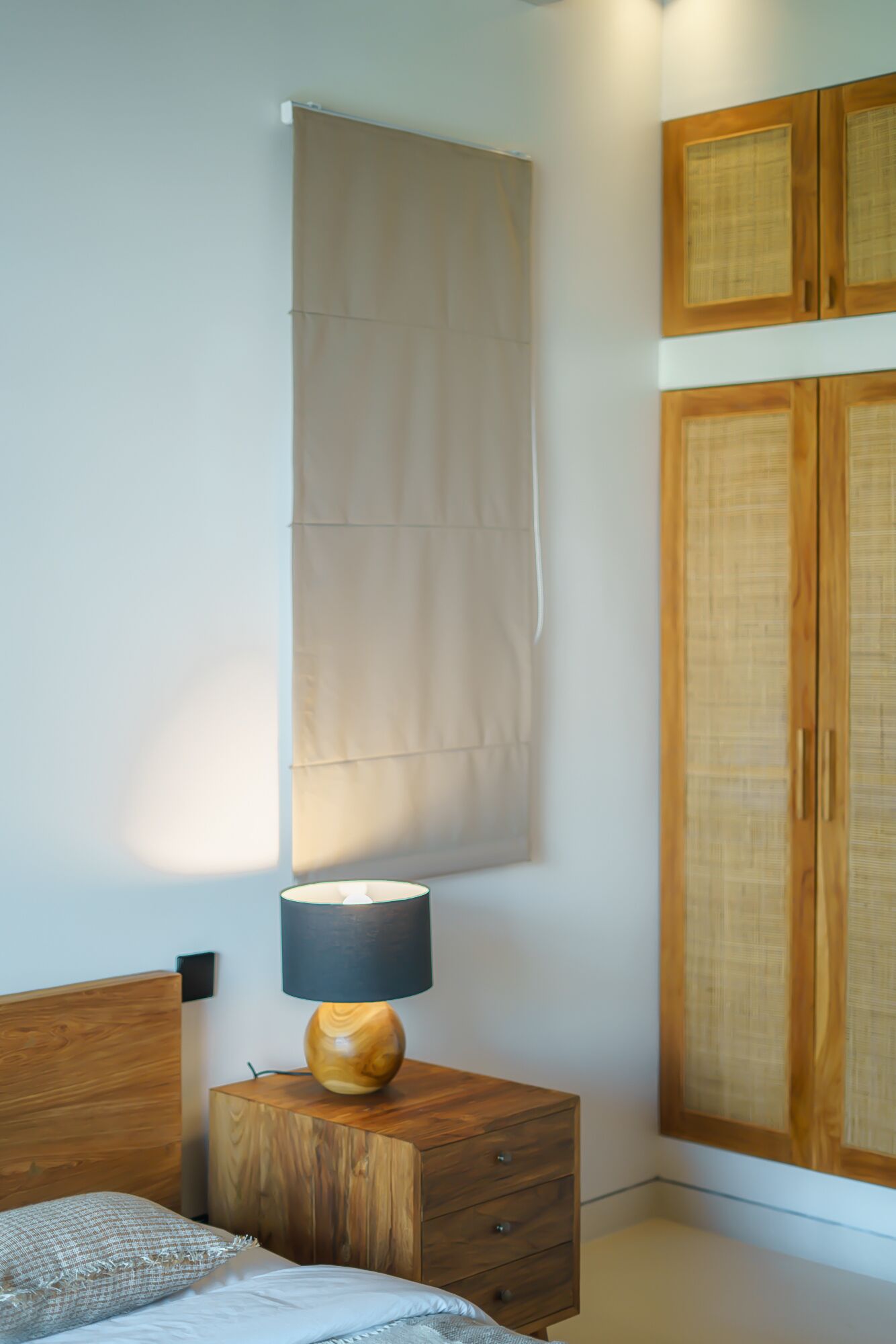 Un dormitorio con cama, mesita de noche de madera con lámpara, armario y ventana con cortina.