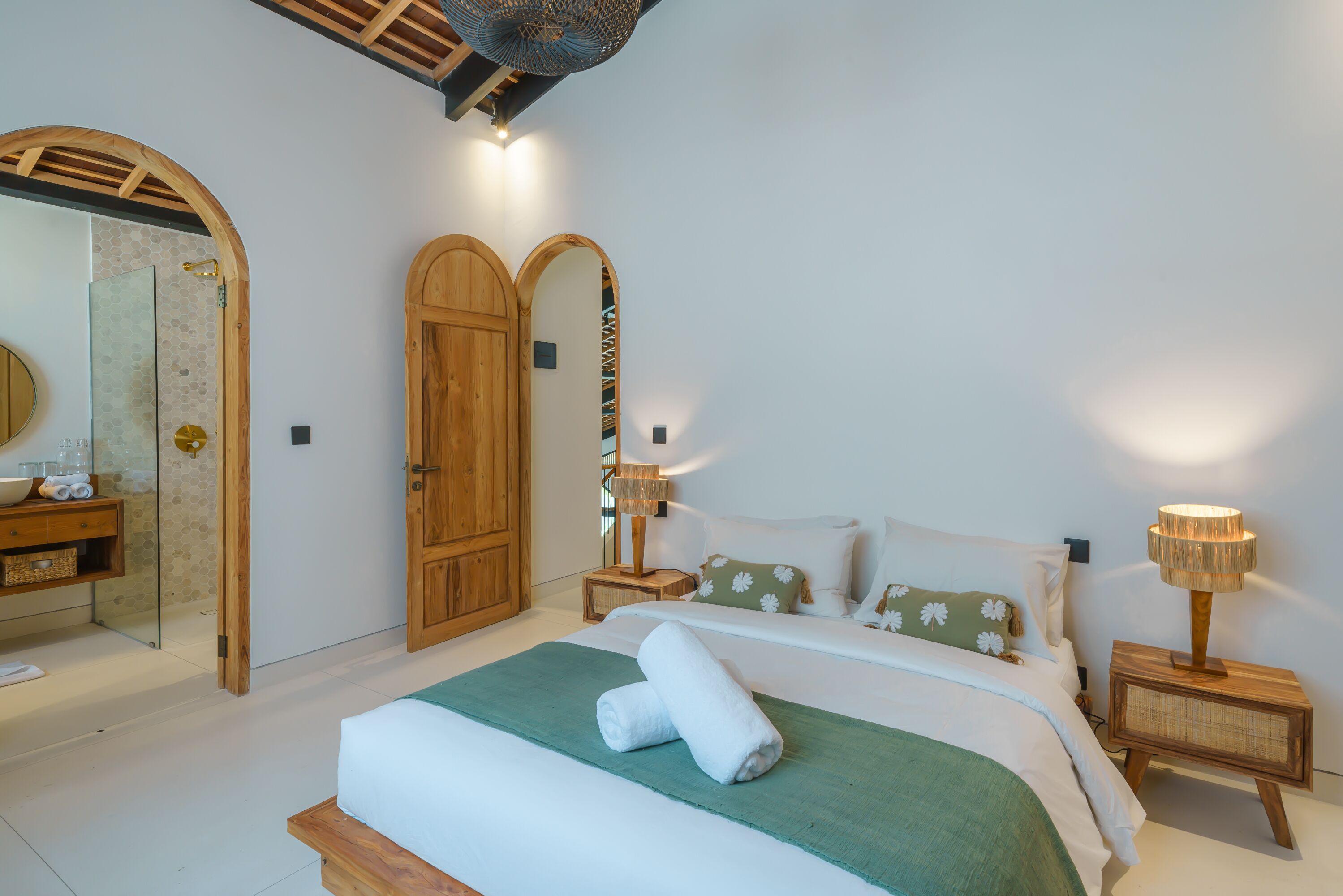 A bedroom with a large bed, wooden wardrobe, and a bathroom with a mirror and sink.
