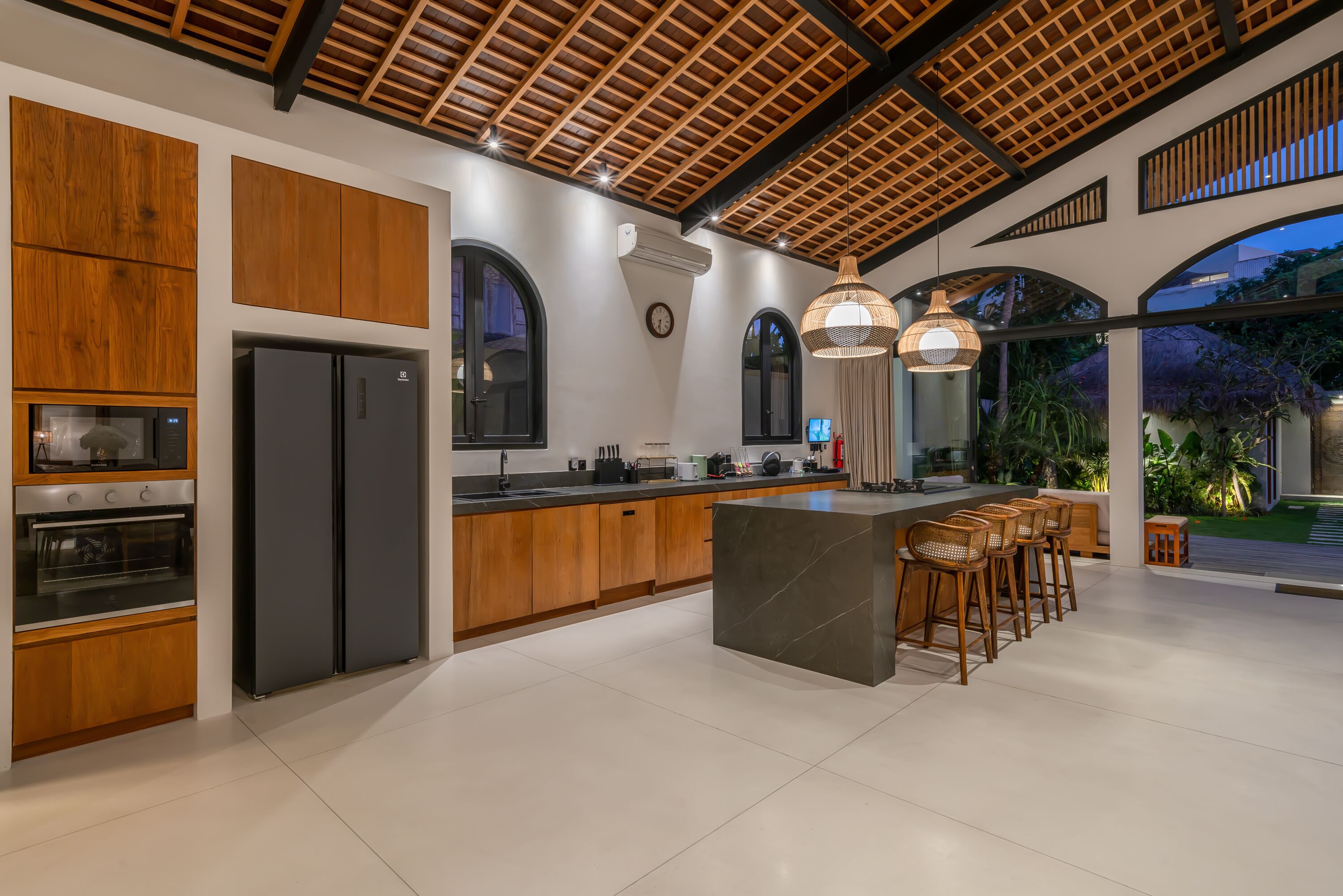 A modern kitchen with wooden cabinets, a black refrigerator, and a large island with bar stools.